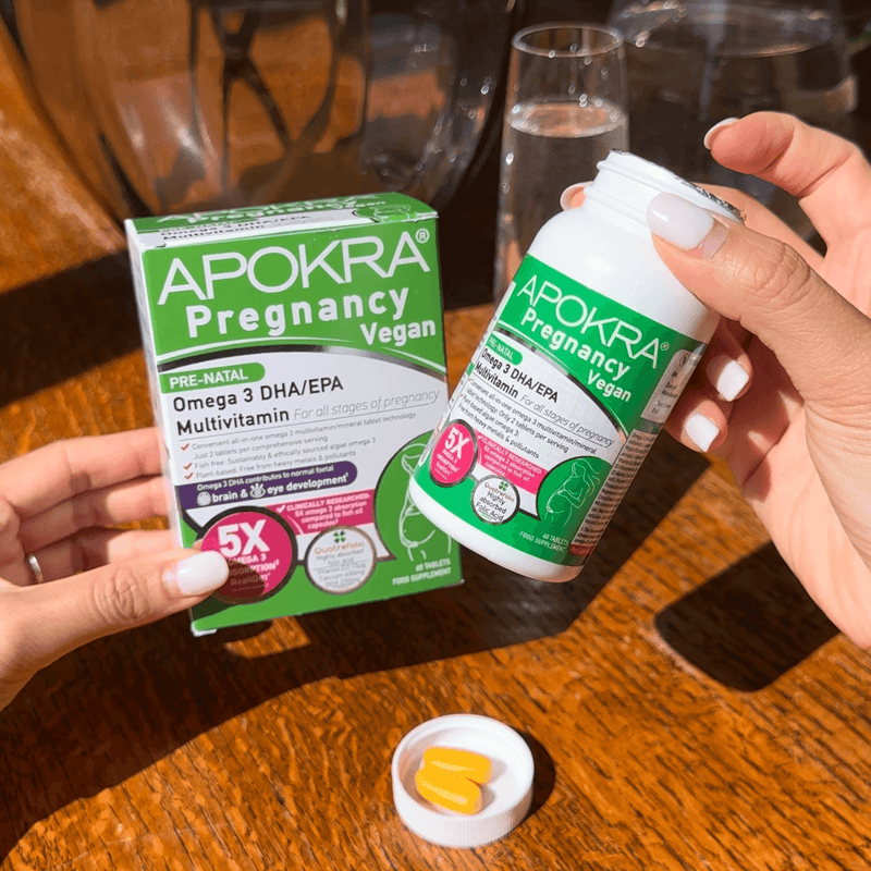 Apokra Pregnancy Vegan multivitamin packaging and bottle on a wooden surface.